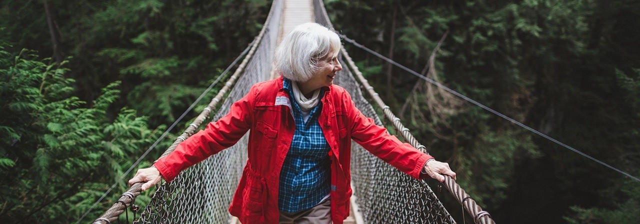 Attractive mature woman walking on suspension bridge through forest